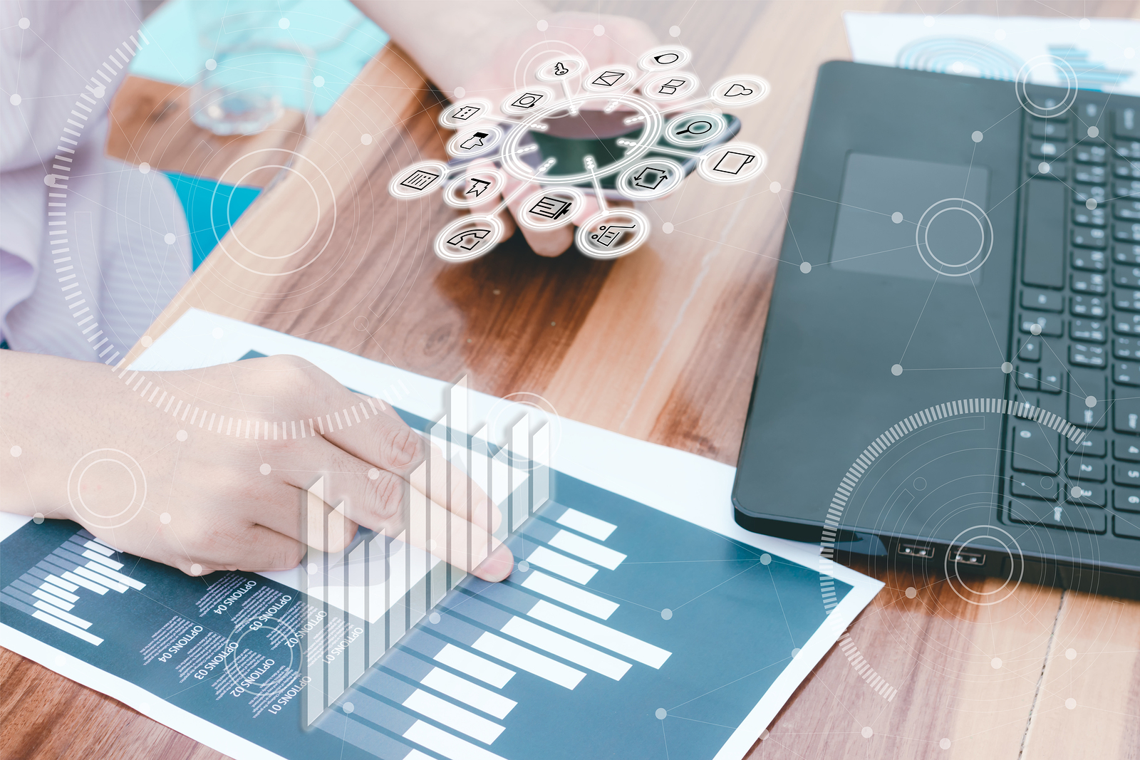 Business woman seated at desk with laptop open, right had on a paper chart, left hand holding a cell phone with augmented reality graphics superimposed on each hand