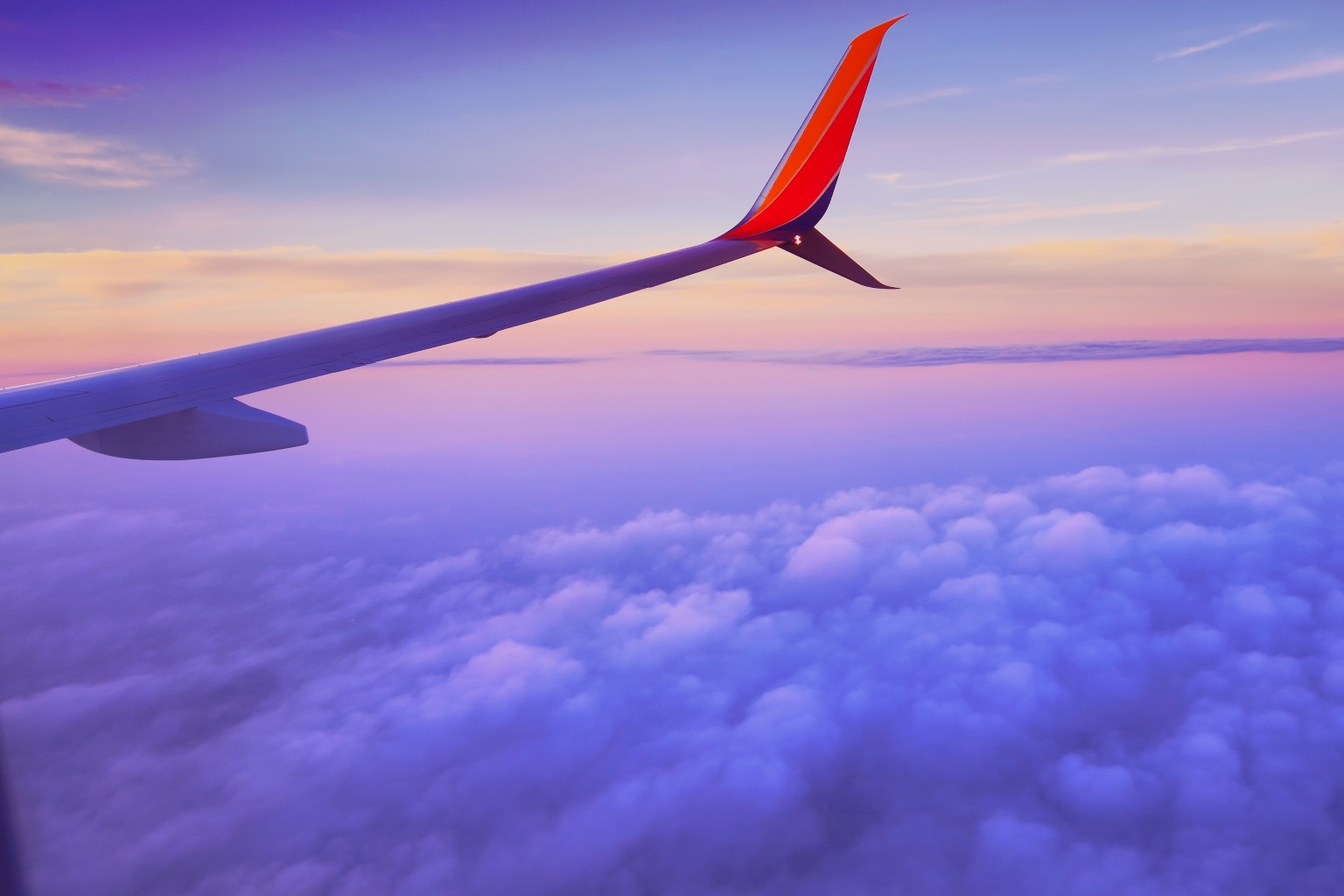From an airplane windows looking out over the wing with the sunset coloring the clouds
